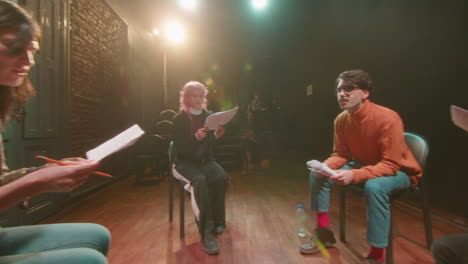 actors sitting in circle on stage and reading scripts during rehearsal