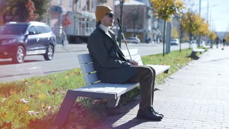 visually impaired man sitting on the bench in the city.