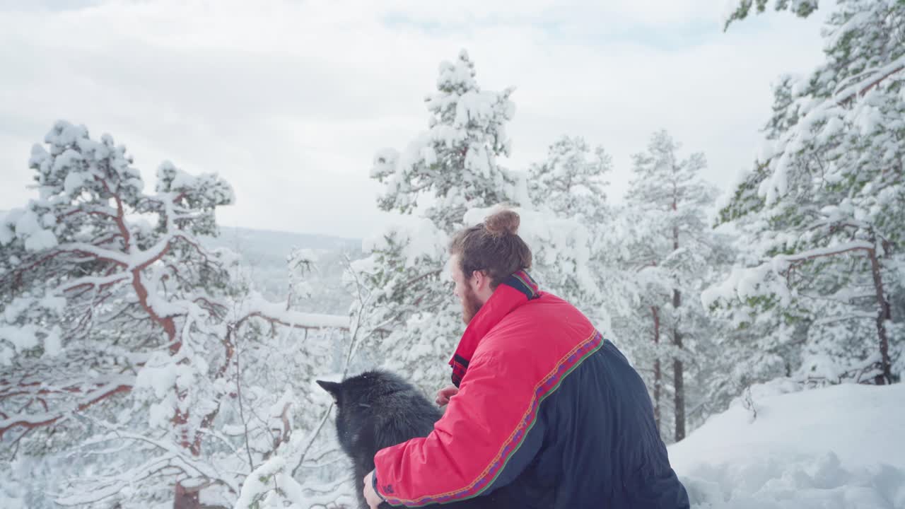 Homem com seu cão Alaskan Malamute sentado em um dia frio de inverno na Noruega - plano médio