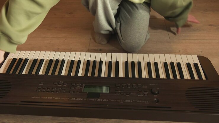 Top down view of person seated cross legged behind electronic keyboard, hands hovering above black and white keys during relaxed pause after playing, inside warm kitchen setting with calm