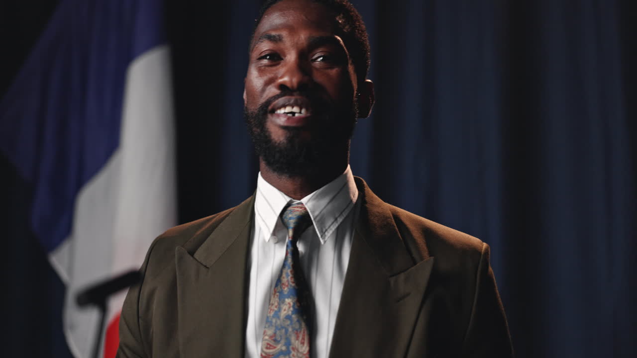 Man in suit speaking near flag
