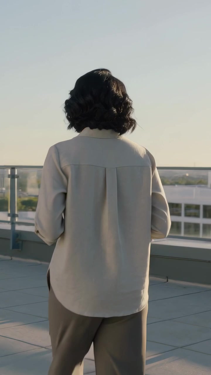 Vertical video: Turning woman in shirt rolled sleeves rooftop observing skyline holding travel mug
