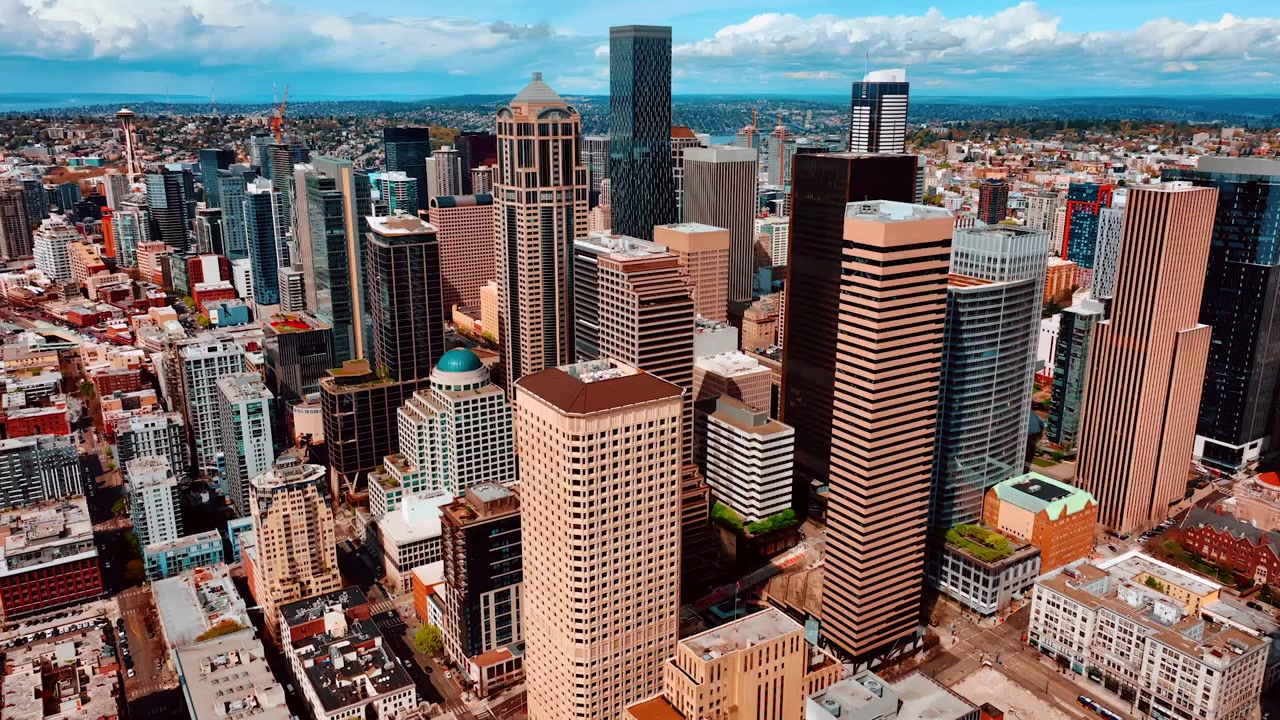 Flying closer to the beautiful modern high-rise buildings in the downtown of Seattle, Washington, US. Sunny cityscape of the metropolis from top.