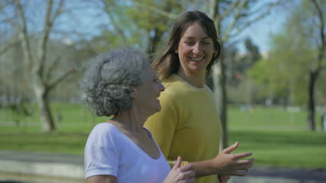 Medium-shot-of-two-women-jogging-in-park,-talking-and-smiling