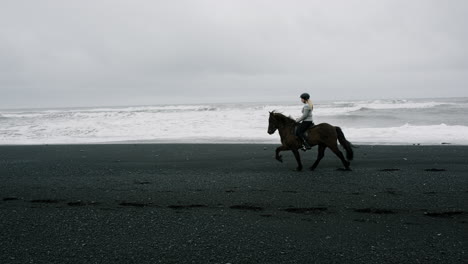 woman horseback riding on a black sand beach in iceland