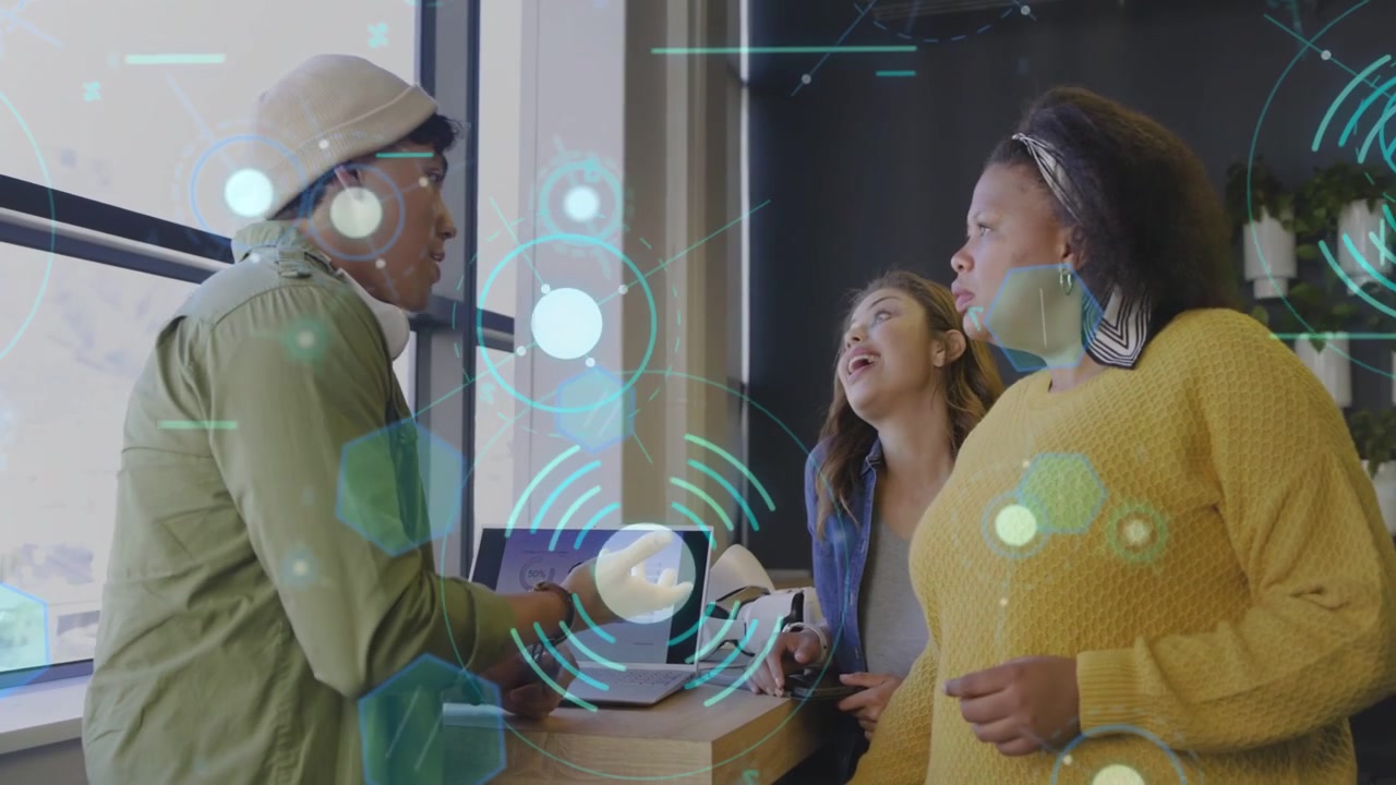 Man leaning, showing laptop to women team for tech demo, blue UI overlay appearing on screen