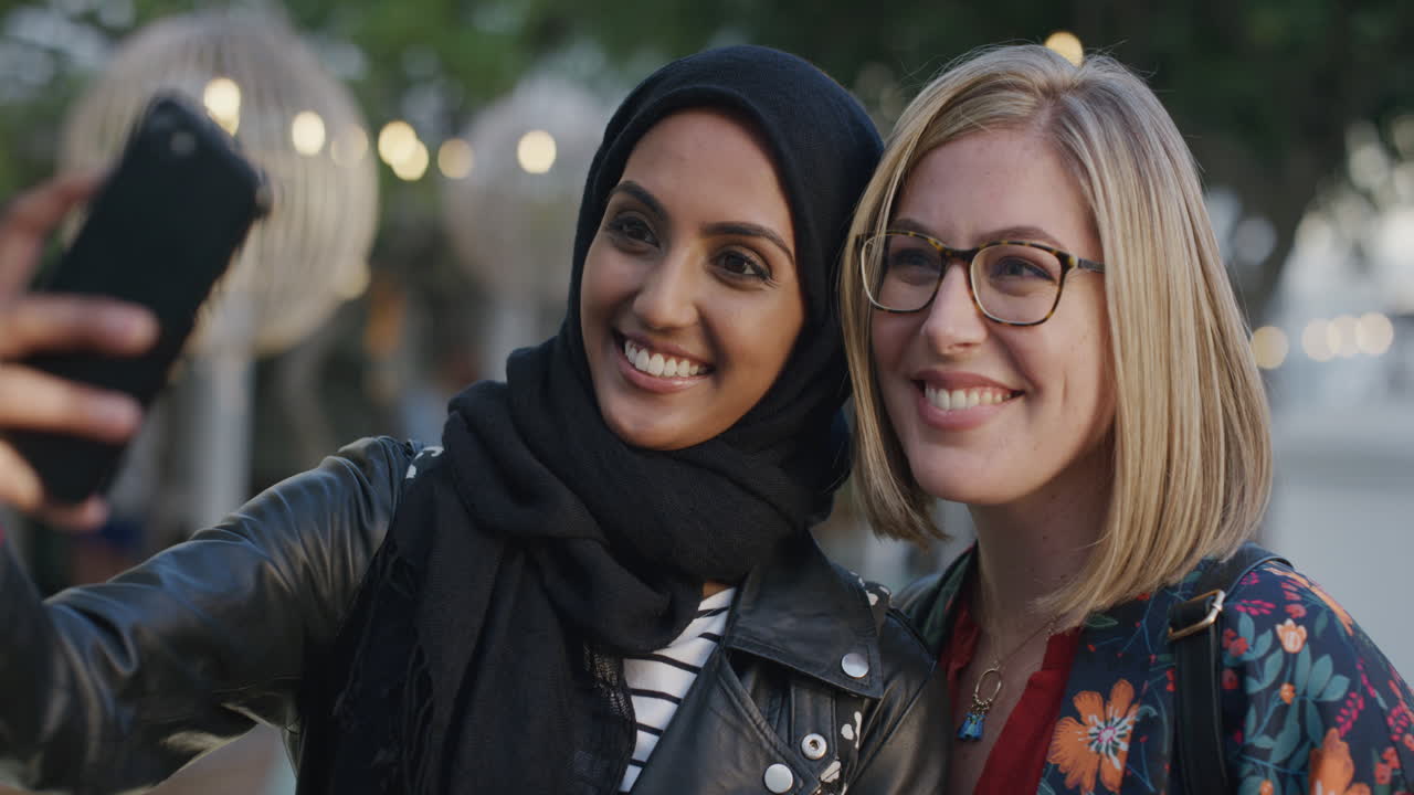 초상화 아름다운 젊은 여성 친구들이 스마트폰 카메라를 사용하여 셀카 사진을 찍고 미소 짓고 휴가를 즐기고 다민족 소녀들이 도시에서 휴대 전화로 재미를 느끼고 있습니다.