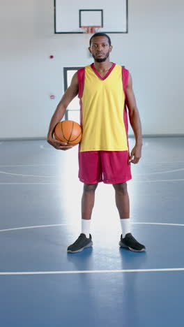 vertical video: holding basketball, male athlete standing on indoor court in sports uniform