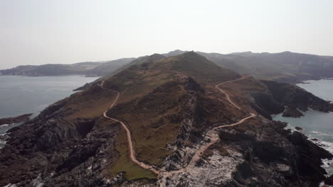 Aerial-Fly-Away-from-Morte-Point-Headland-in-North-Devon,-Tilting-Down-Towards-the-Ocean-with-Birds-Flying-Past