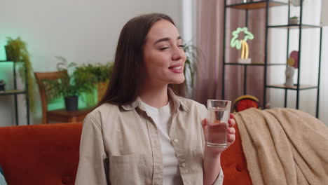 Thirsty-young-woman-sitting-at-home-holding-glass-of-natural-aqua-make-sips-drinking-still-water