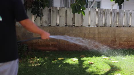 Joven-Bronceado-Regando-El-Patio-Trasero-Con-Una-Manguera-De-Jardín-En-Un-Día-Caluroso