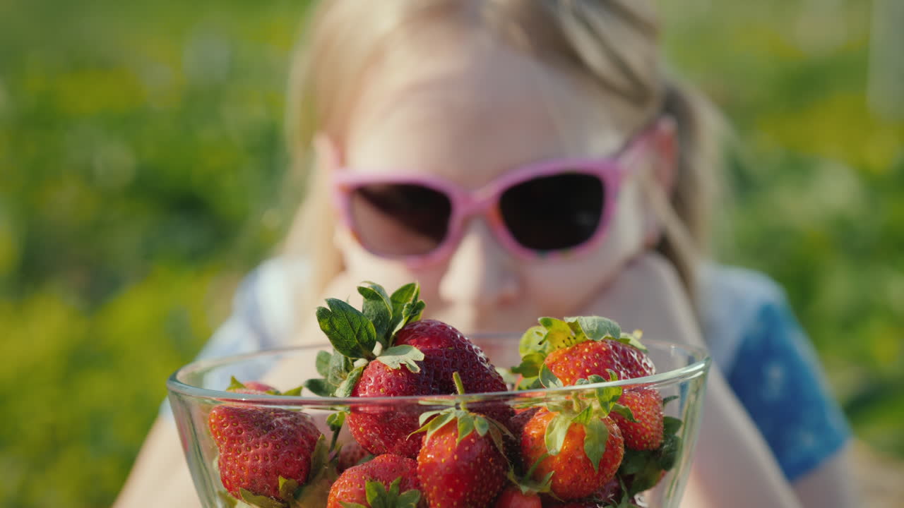 선글라스를 쓴 소녀는 잘 익은 딸기 한 그릇을 본다 1
