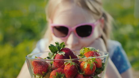 chica con gafas de sol mira un tazón de fresas maduras 1