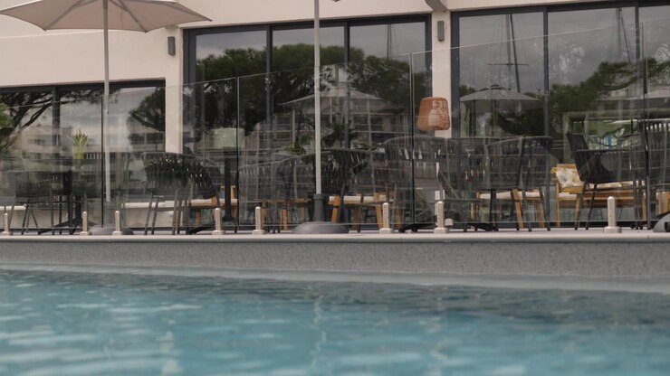 Outdoor swimming pool beside a glass safety fence and furnished terrace outside a modern building
