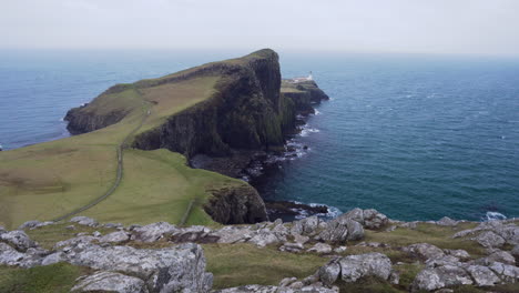 Tilt-up-shot-of-Neist-Point-lighthouse-with-rocky-cliffs-in-foreground-and-Atlantic-Ocean-in-the-background-on-a-windy-and-cloudy-day-in-Scotland,-Isle-of-Skye