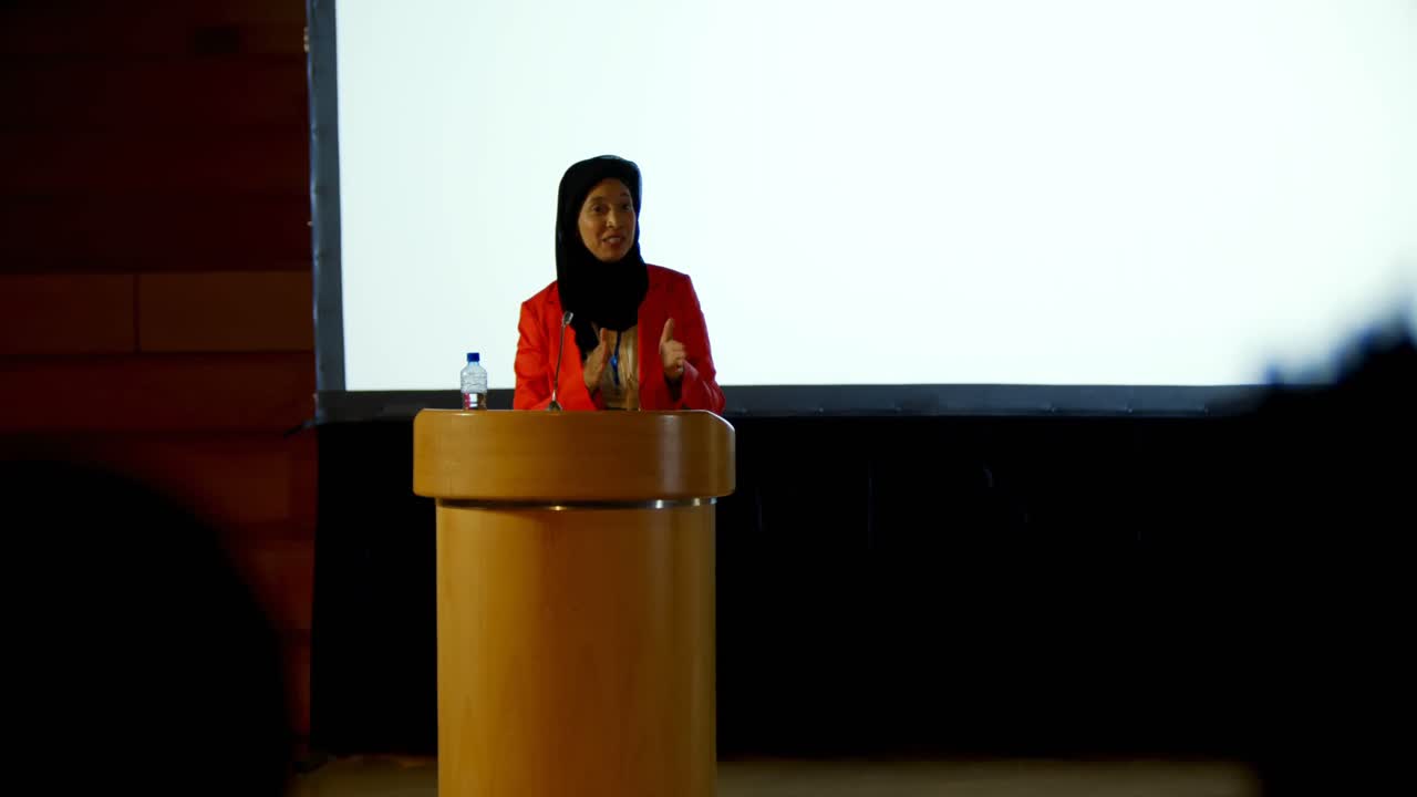 Mature Caucasian hijab businesswoman speaking at podium in auditorium 4k