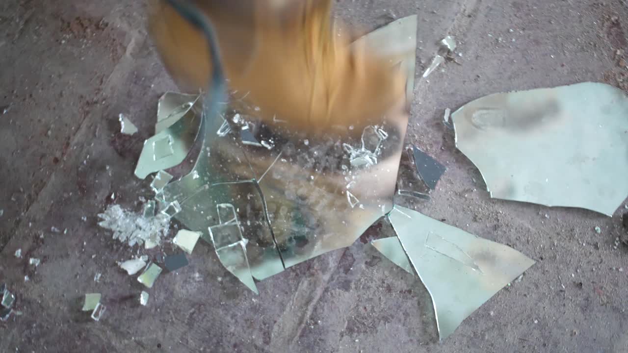 한 젊은 여성이 더럽고 먼지가 많은 콘크리트 바닥에 부츠를 신고 자신의 모습을 보여주는 거울 조각을 부수고 있다