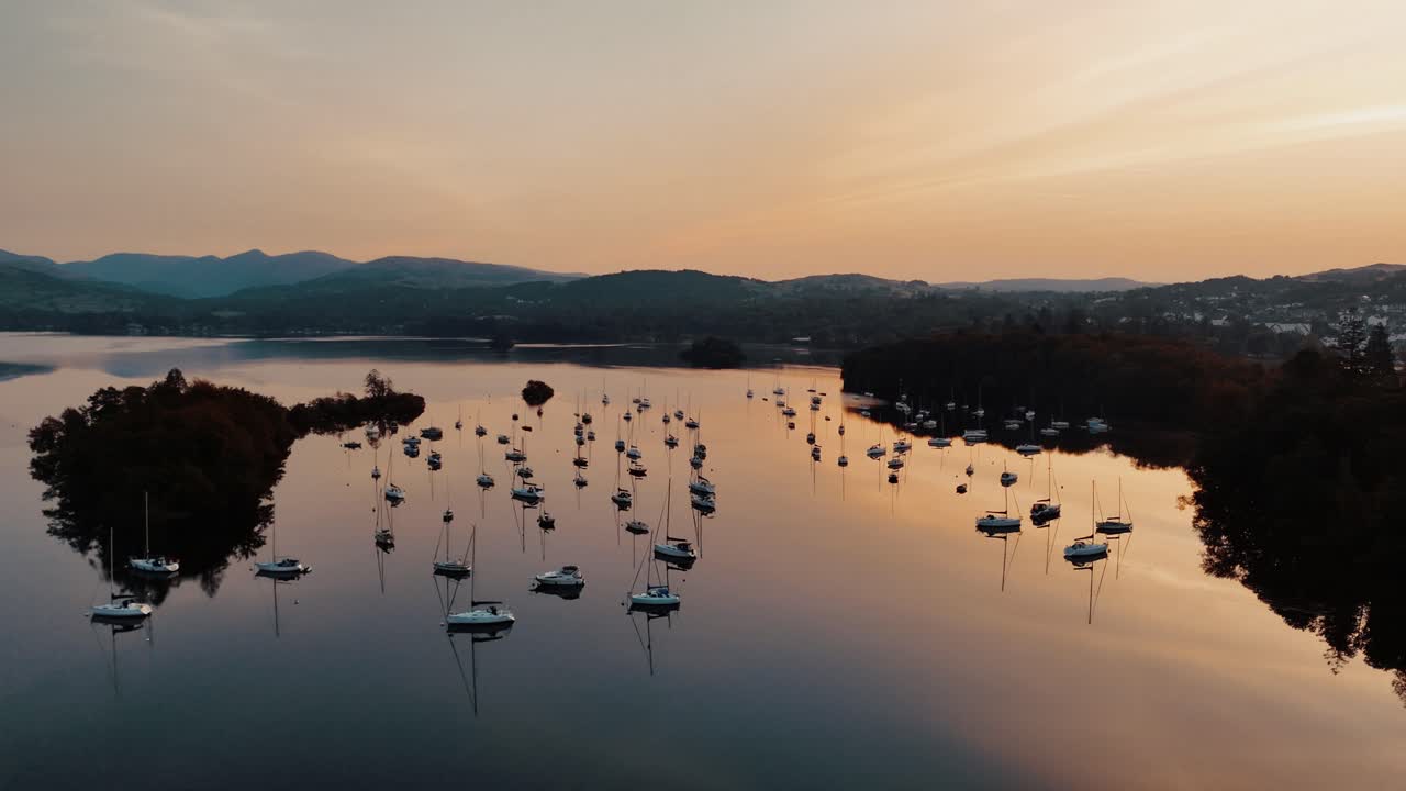 Wide aerial circle right of sailboats reflecting bright orange sunrise on Windermere Lake