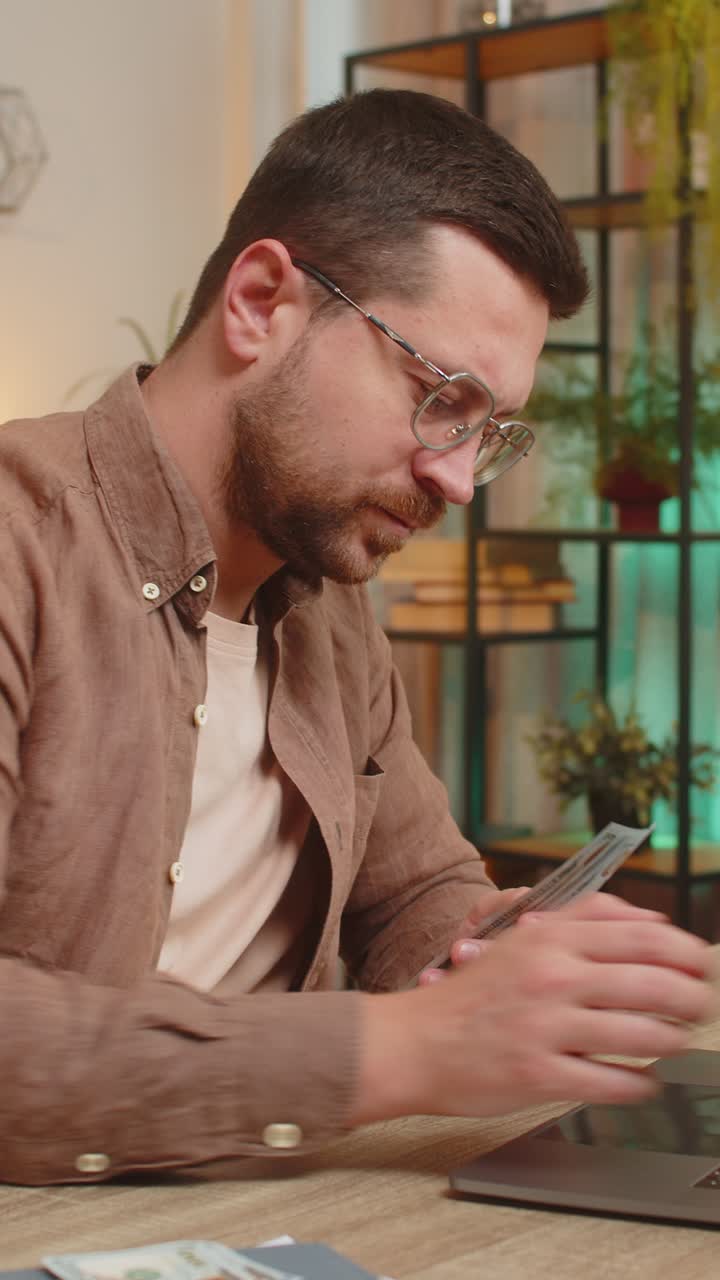 Rich happy caucasian man counting money cash using laptop calculate domestic bills at home table