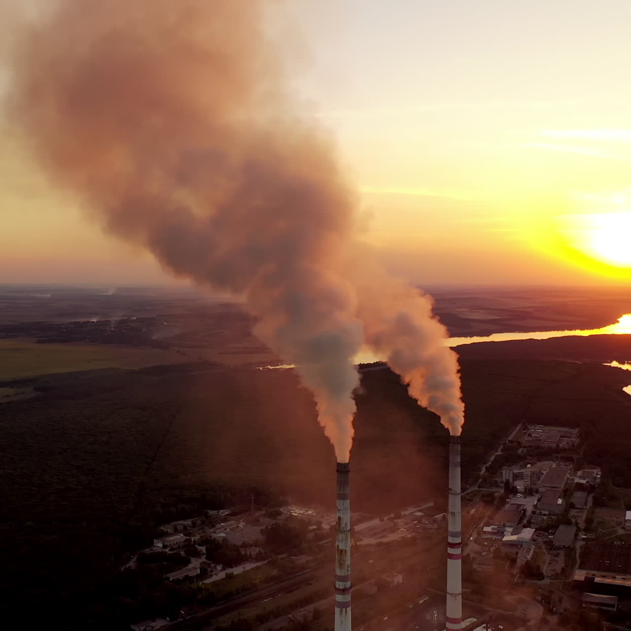 Metallurgical plant at sunset. Smoke coming out of factory pipes on the natural background. Aerial view. Camera moves back.