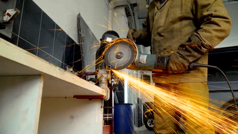 primer plano de un trabajador que utiliza una molienda para cortar metal en un taller