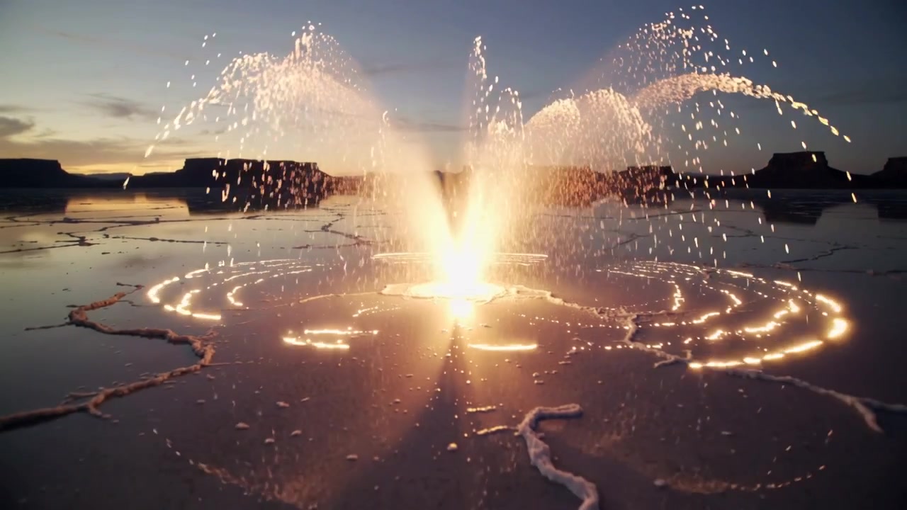 Bright point igniting pyrotechnic fountain sending jets and glowing rings across salt flat at dusk
