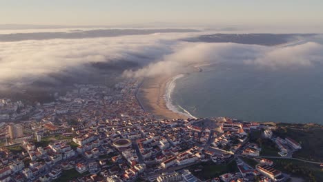 Time-lapse-of-Coastal-city-of-Nazare-Portugal-during-sunrise-with-low-clouds,-aerial