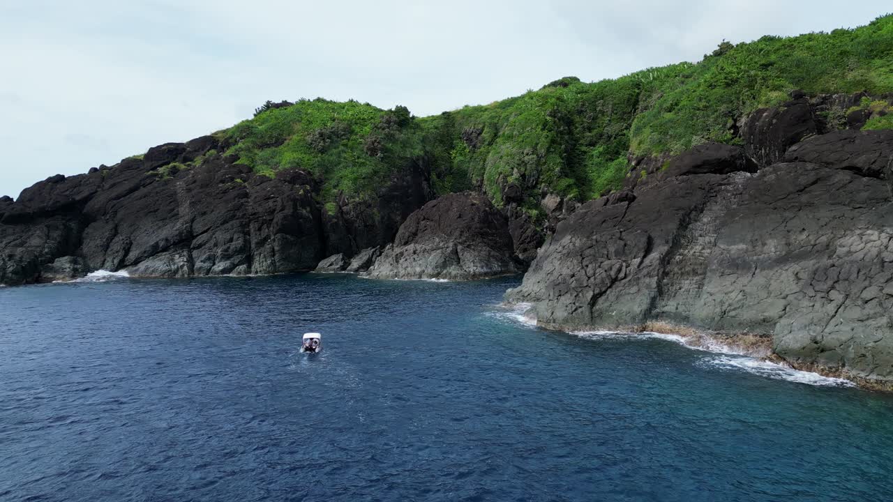 Flyover Shot of Inflatable Zodiac Boat traveling in tropical island lagoon with large jagged boulders and turquoise ocean waters