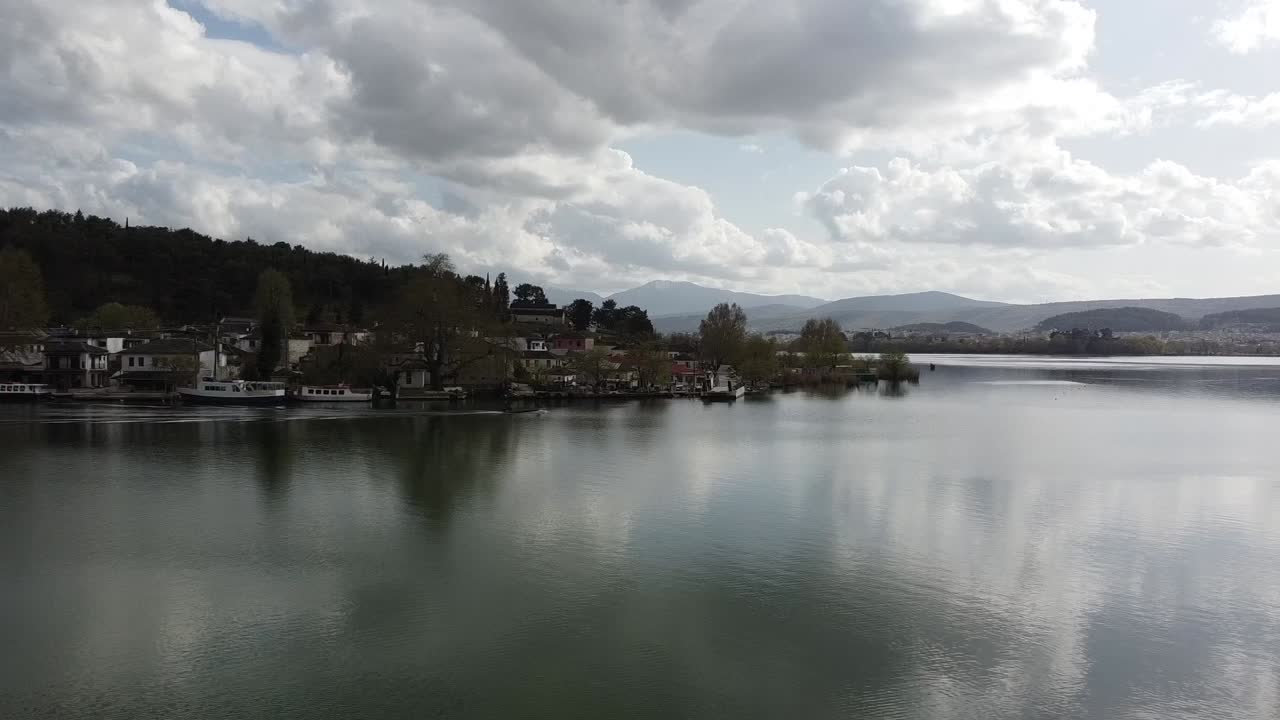 Luftaufnahme aus geringer Höhe, die über die ruhige Oberfläche des Pamvotida-Sees auf die traditionelle Siedlung der Insel Ioannina zufliegt. Malerische Ansicht der Dorfhäuser und des Seeufers in Griechenland