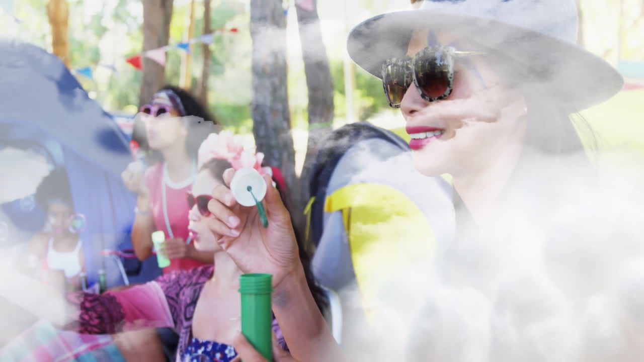 Blowing bubbles at picnic, women with colorful decorations and trees surrounding