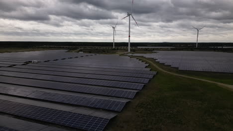 Stormy-clouds-above-solar-panels-and-wind-turbines,-aerial-fly-backward