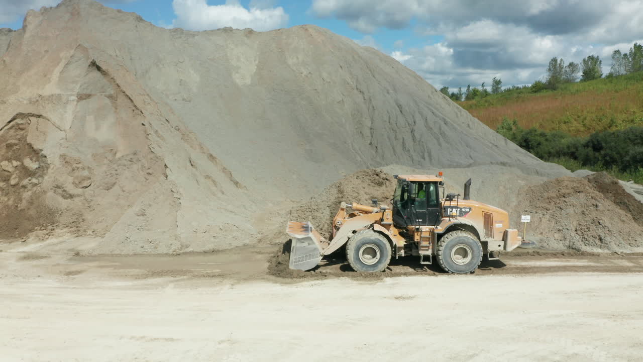 vista lateral del cargador delantero empujando la piedra caliza para formar una gran pila en la cantera