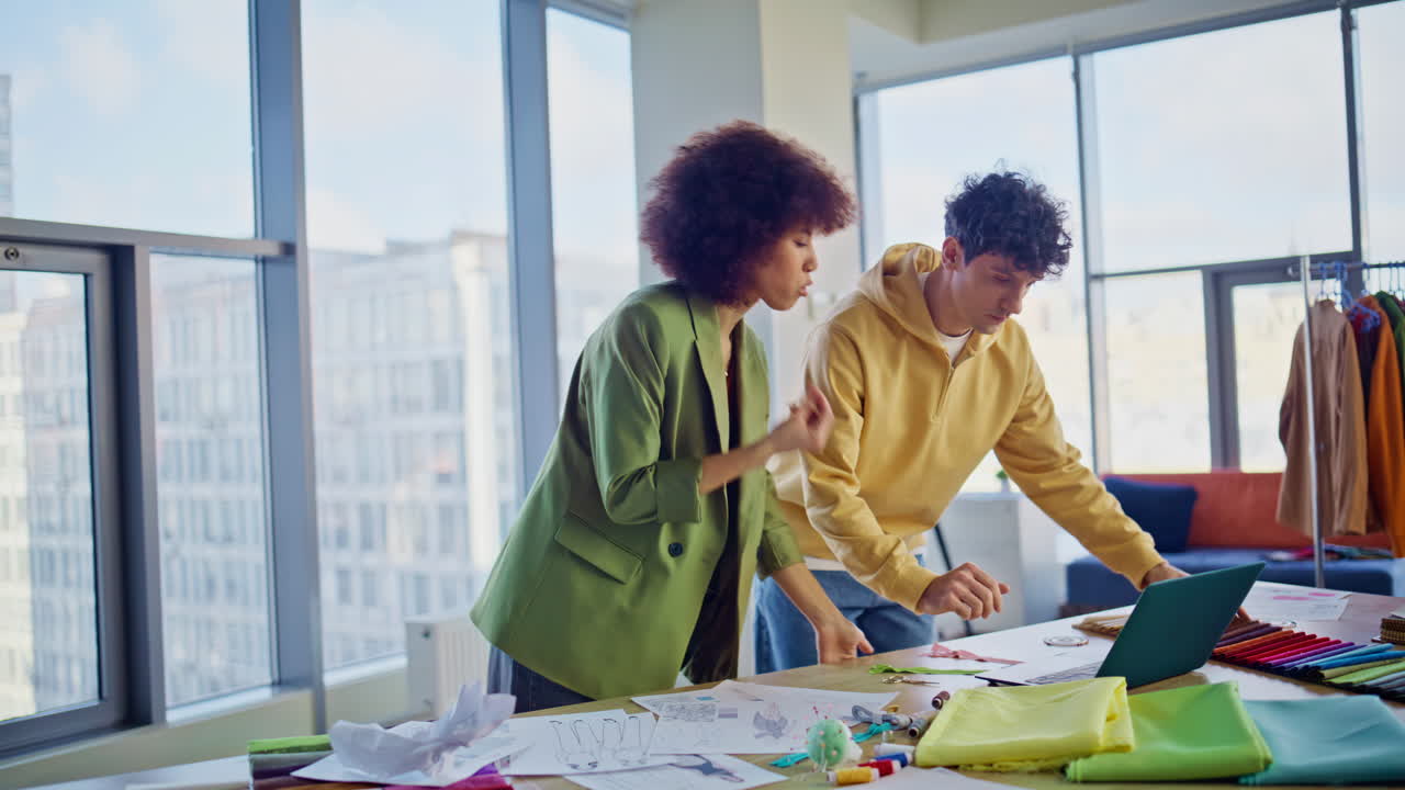Tailors discussing design problem looking laptop in fashion studio workspace
