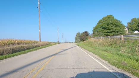 POV-driving-past-mature-corn-fields,-soybean-fields-and-farmyards-in-rural-Iowa-on-a-sunny-early-autumn-day
