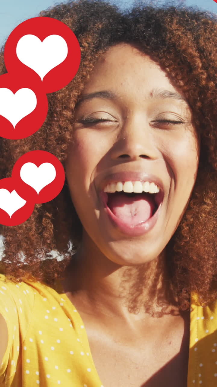 Animation of red heart love digital icons over smiling woman blowing kisses on beach
