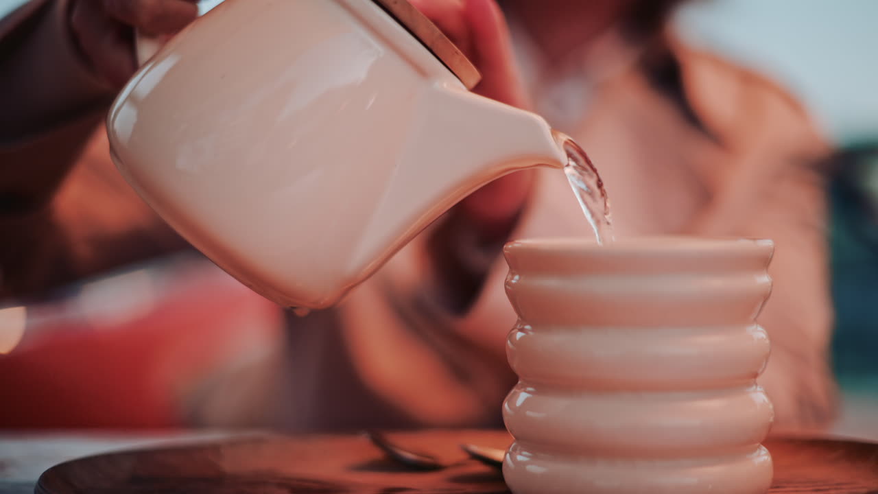 A woman pouring tea into a ceramic cup, filmed in warm evening tones