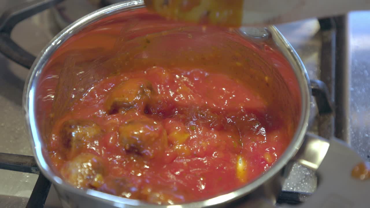 disparo de primer plano de albóndigas en una salsa de tomate que se agita con una cuchara de madera