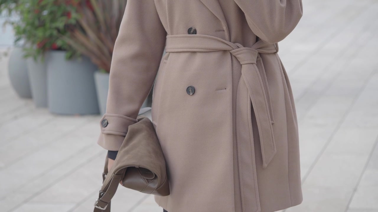 Donna elegante che indossa un cappotto beige e porta una borsa