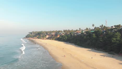 Varkala-shoreline-bathed-by-the-Arabian-sea-on-the-Malabar-Coast,-in-Kerala,-India---Aerial-Low-angle-slow-slide-shot