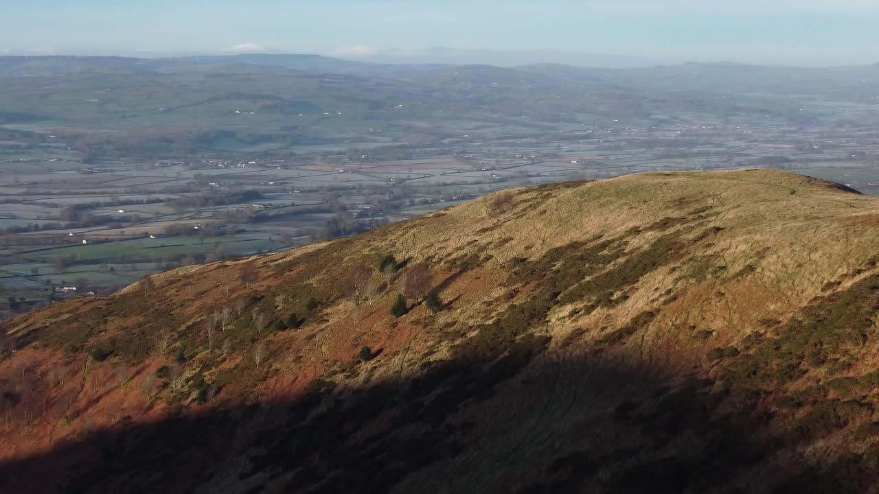 la primera luz del sol en el pico de la montaña de las tierras altas vista aérea a través de vastas y heladas idílicas tierras de cultivo galesas pan derecho