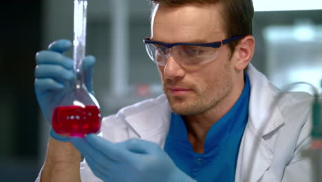 químico en el laboratorio. primer plano de un químico masculino mirando líquido en un frasco de vidrio