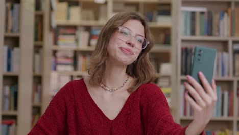 Niña-Feliz-Saluda-Mientras-Chatea-Por-Video-Con-El-Teléfono-En-La-Biblioteca,-Slomo