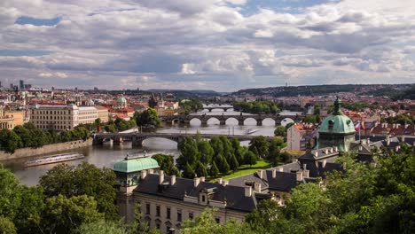 Cloudy-afternoon-timelapse-of-the-Vltava-river-in-Prague,-Czech-Republic-from-Letná-park-as-clouds-and-boats-pass-by-on-a-summer-day-with-Strakovská-akademie-and-Charles-Bridge-in-frame