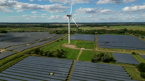 a windturbine is spinning in the middle of a solar farm on a green field