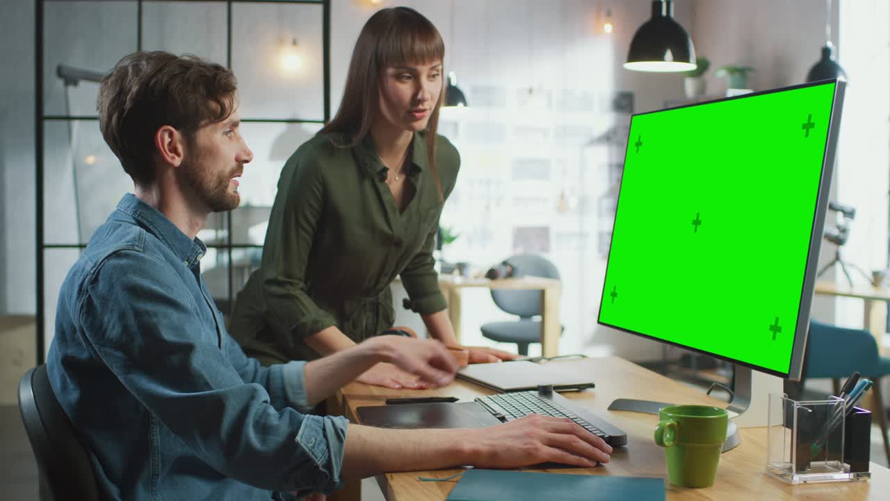 directora de arte femenina consulta a su colega diseñador, trabajan en una computadora personal con pantalla verde. trabajan en un loft de oficina genial. se ven muy creativos y geniales.