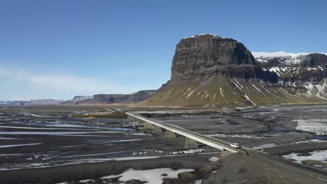 cruce de vehículos en un puente de un carril que cruza el río nupsvotn con vistas a la montaña lomagnupur