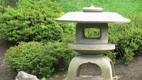 una linterna de nieve japonesa se encuentra en medio de arbustos de azalea en un jardín japonés