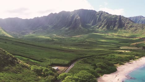 aerial drone footage of winding coastal road along sandy beach at hai van pass in central vietnam, showing lush green mountains, turquoise sea, roadside trees and panoramic view under clear sky