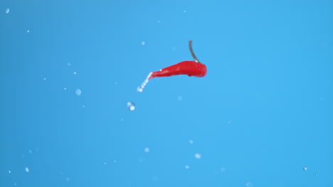 single small chili jumping up, making half a rotation and spinning with water droplets