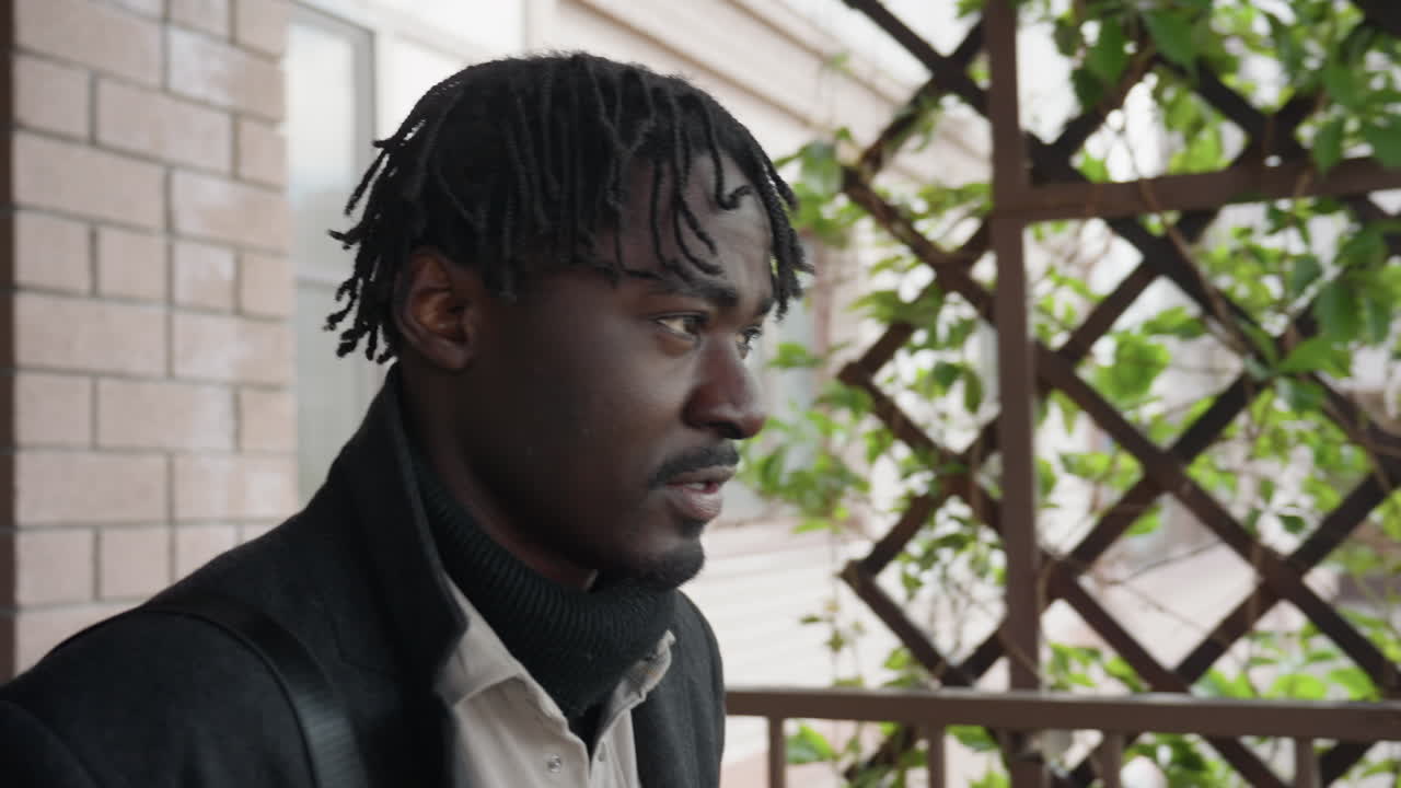 Un hombre adulto con barba redonda y espinillas en la mejilla se golpea la frente con la mano, mira hacia afuera, su expresión muestra arrepentimiento, tiempo perdido, autorreproche, pausa reflexiva cerca de la entrada y un momento interior auténtico.